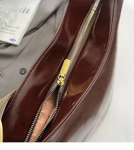Close-up of smooth gold metal zipper and dark brown patent leather on a fashion handbag