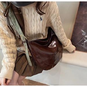 Detail of a large dark brown polished PU leather hobo bag with adjustable strap
