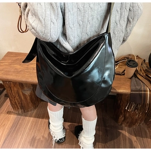 Chic black patent leather crescent bag worn with casual autumn sweater and wooden bench