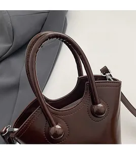 Detail of dark chocolate handbag featuring round handles and silver metallic hardware hooks