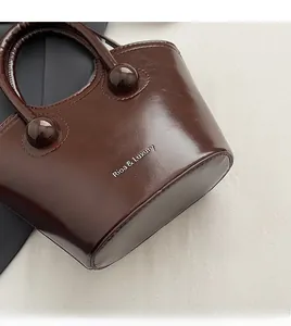 Detail of a brown oil-wax leather bucket bag with shiny texture and top handle