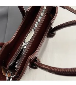 Close-up of smooth metal zipper and leather handle on a burgundy bucket bag