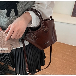 Detail of dark brown glossy leather bucket bag with top handle worn by a model