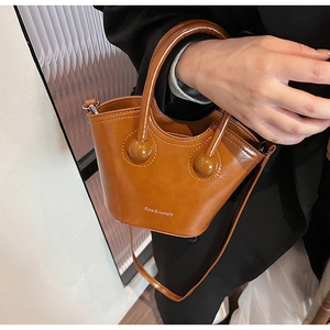 Detail of a brown glossy leather bucket bag with top handles and logo lettering