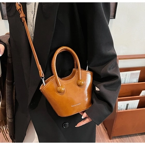 Close-up of brown patent leather wing-shaped handbag with Rioa & Luxury logo and shoulder strap