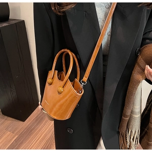 Detail of caramel brown mini bucket bag with spherical hardware and leather handles