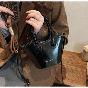 Close-up of black glossy bucket bag with ball handles and Rioa & Luxury logo details