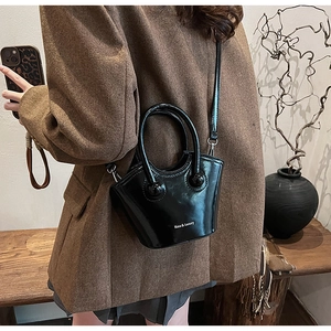 Detail of high-gloss black patent leather bucket bag with white brand logo and top handles