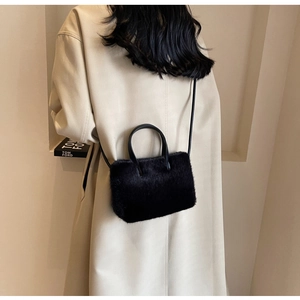 Sac à main minimaliste en peluche noire avec bandoulière porté sur un manteau beige