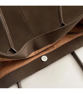 Detailed close-up of a magnetic circular metal snap closure on a brown suede tote bag