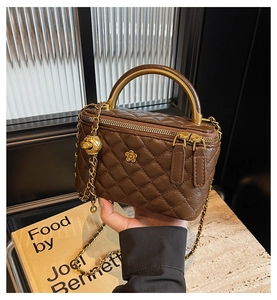 Detail of a brown quilted leather box bag with a golden circular handle and chain strap