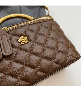 Detailaufnahme einer dunkelbraunen Steppledertasche mit goldenem Griff und Blumenverzierung