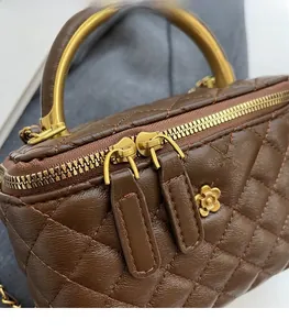 Details der braun gesteppten Kosmetiktasche mit goldener Kamelie und rundem Metallgriff