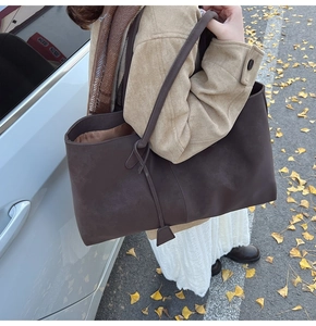 Deep brown suede tote bag featuring a decorative knotted shoulder strap detail in a fall setting