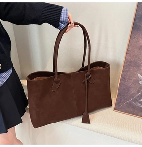 Detailed view of deep brown suede tote bag featuring long handles and matching charm