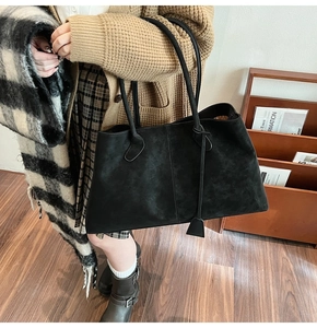 Black suede tote bag with metal clasp and sleek shoulder straps for women on wood floor