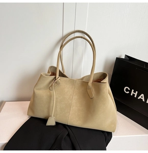 Detail of light khaki matte tote bag with long shoulder strap on a white table