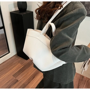 Side view of a large cream tote bag showing lychee grain leather on green corduroy blazer
