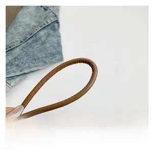 Detailed view of a brown leather shoulder strap with fine stitching on denim background