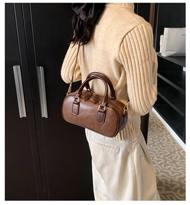 Model wearing dark brown leather Boston bag with gold metal hardware and shoulder strap