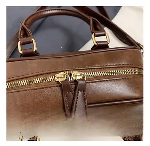 Detail view of the vintage brown leather bag featuring golden dual zippers and sturdy hardware
