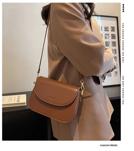 Detail of a brown matte leather flap crossbody bag with golden metal hardware and branding