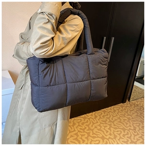 Detail of a large quilted down tote bag in dark grey nylon shown on a model