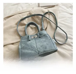 Detail of light blue crossbody bag with silver twist lock and rivet accents on beige fabric