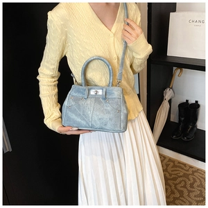 Detail of light blue denim texture handbag with silver twist lock and studs worn by model