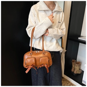 Detail of brown faux leather shoulder bag with decorative bows and zipper pockets