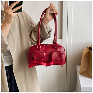 Detail of red leather shoulder bag featuring ribbon bows and silver zippers on model