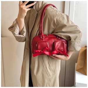 Detail of red cylinder PU leather handbag featuring two front pockets and decorative ribbons