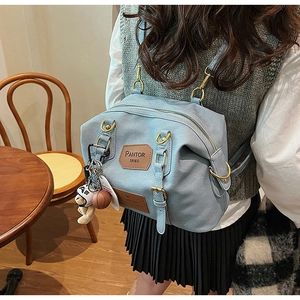 Detail of light blue denim backpack featuring brown leather logo and cute teddy bear charm