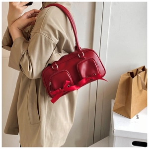 Detail of red PU leather shoulder bag featuring ribbon bows and functional zipper pockets