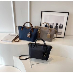 Three-color trapezoid nylon tote bags displayed on white pedestals with leather handles
