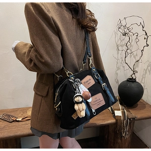 Close-up of black denim versatile bag featuring leather patches and plush bear charms
