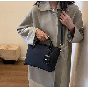 Detail of black nylon tote bag with leather handles shown on a beige trench coat