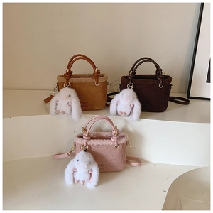 Détail de sacs seaux mats avec bordure en fausse fourrure, anses en cuir et breloque lapin