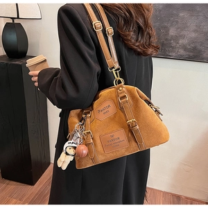 Detail of a brown suede crossbody bag with vintage leather patches and a cute bear charm