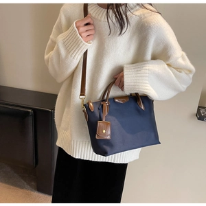Detail of navy nylon crossbody bag featuring brown faux leather handles and metal hardware