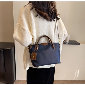 Detail view of large navy Oxford tote bag with brown leather handles worn by a model