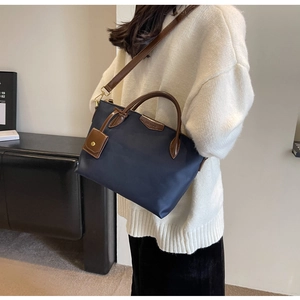 Detail of navy nylon tote bag with brown leather handles worn by a female model