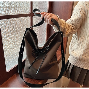 Detail of soft brown suede shoulder bag with black leather bow and adjustable strap