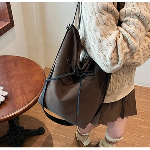 Détail du grand sac bandoulière en daim marron café avec nœud décoratif en ruban noir