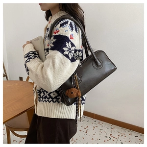 Model wearing dark brown leather baguette bag with plush bear charm and vintage knitwear