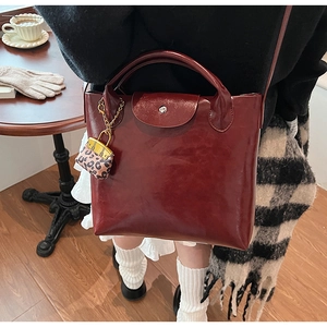 Detail van een bordeauxrode leren tas met luipaardprint bedeltje in een gezellige herfstsfeer