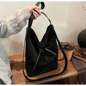 Détail du sac seau en daim noir avec nœud en cuir sur une table en bois rustique