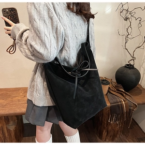 Close-up of black suede tote bag with stylish bow knots on shoulder straps and spacious design