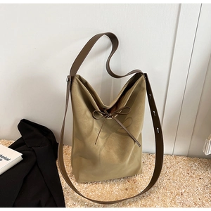 Detail of khaki canvas bucket bag with decorative bow and brown leather shoulder strap