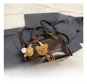 Detail of dark brown leather handbag with a plush bear charm and baseball glove decor